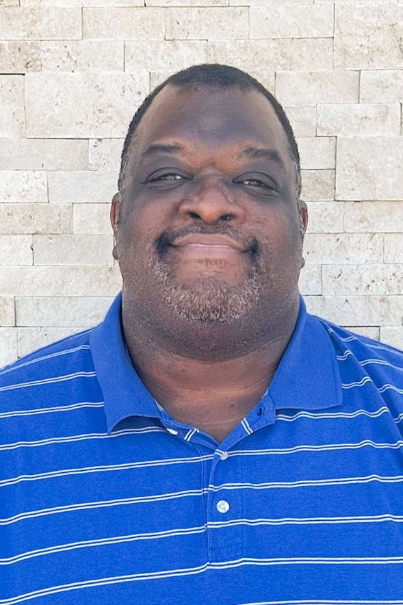 Portrait of a smiling man in a blue striped polo shirt against a brick wall.